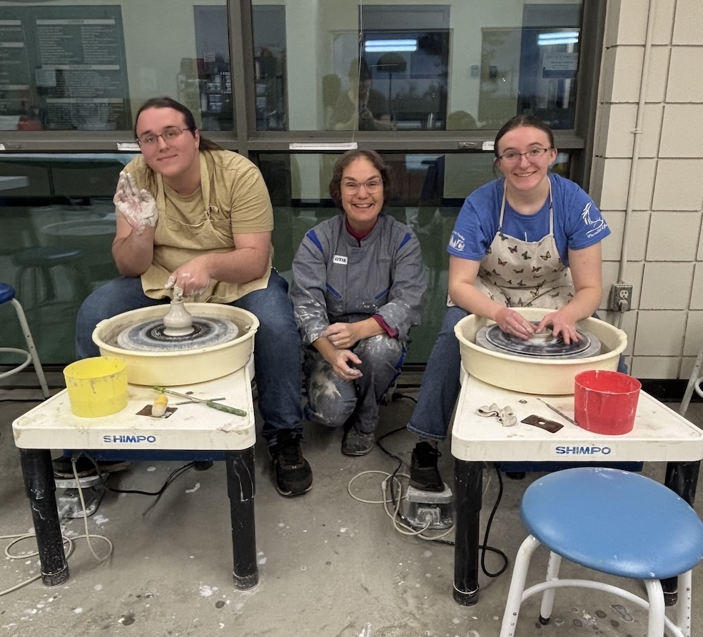Three women in an art class happily creating small objects by shaping colorful wool fibers